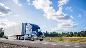 Big rig powerful professional industrial blue bonnet semi truck for long haul delivery commercial cargo going with refrigerator semi trailer on the summer road with forest and meadows on the sides